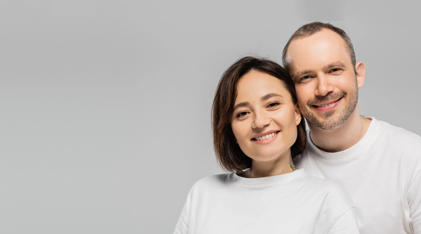 happy husband and wife with short brunette hair standing together in white t-shirts and looking at camera